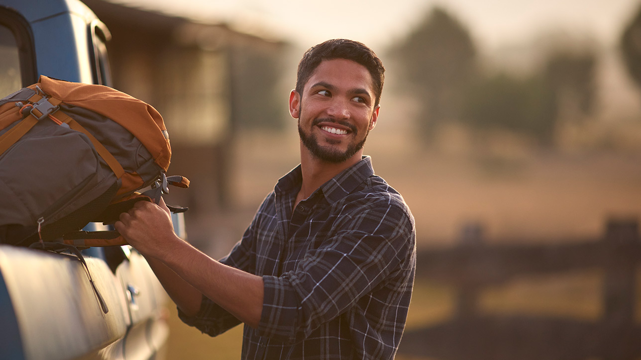 Young man loading backpack into pick up truck